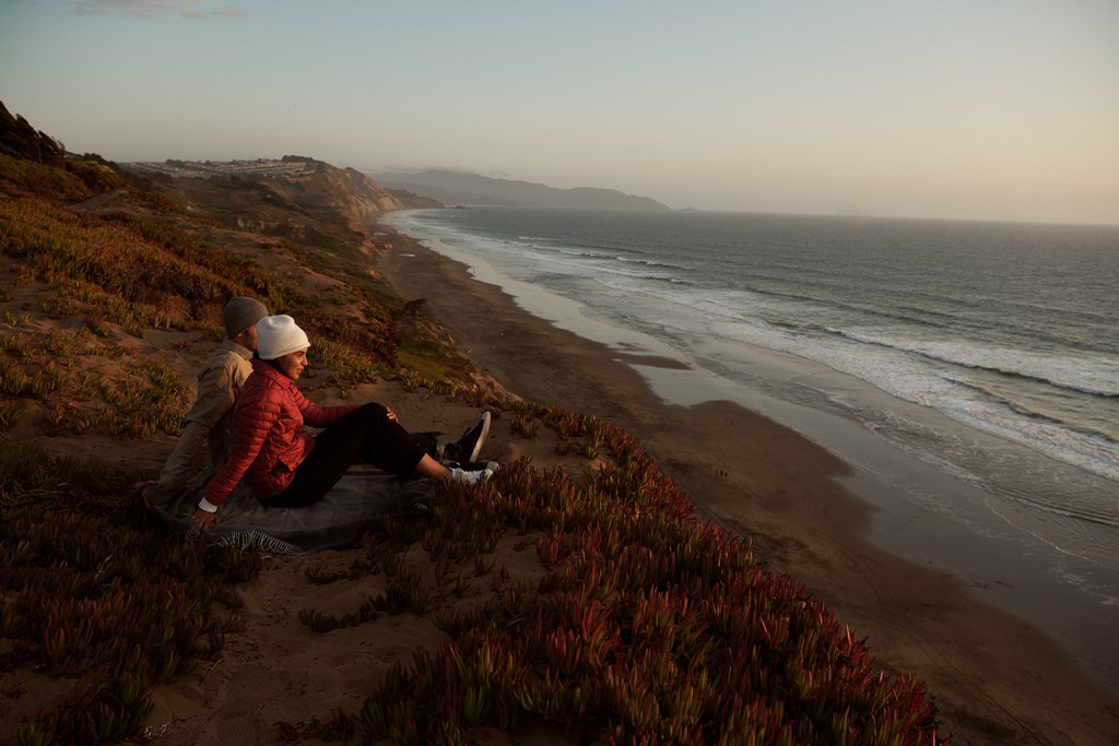 two people sitting on a hill overlooking the beach