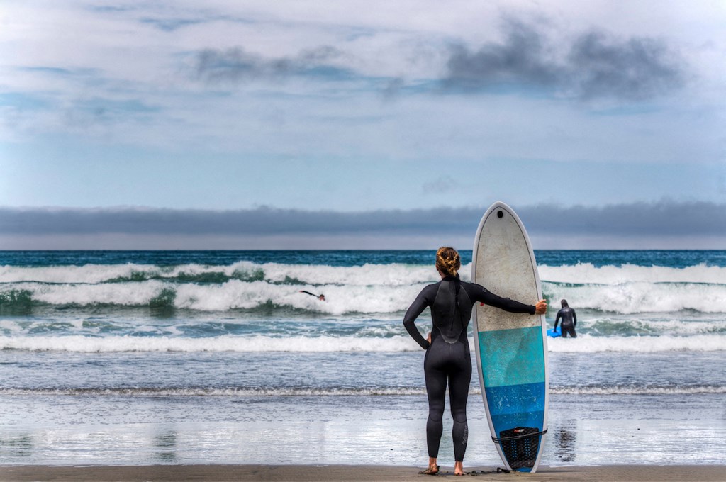 a woman in a wet suit holding a surfboard on the beach