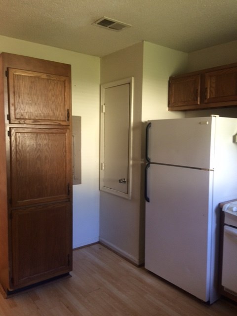 A white refrigerator sits next to a wooden cabinet in a kitchen.