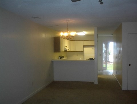 an empty living room with a kitchen and a chandelier