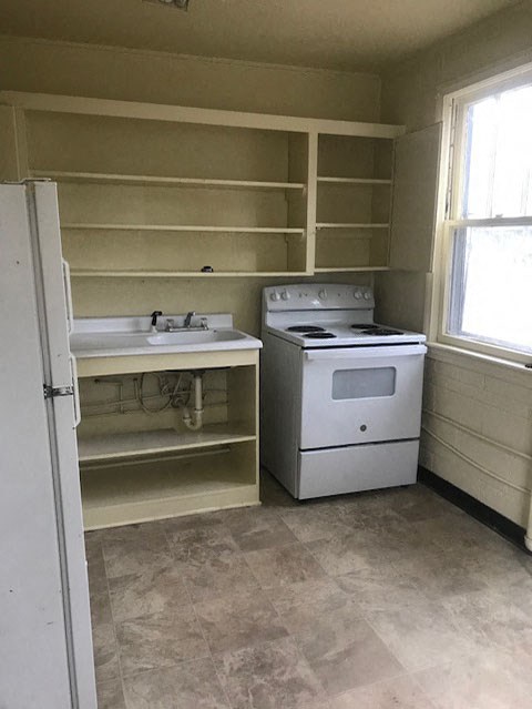 A kitchen with a stove, sink, and shelves.