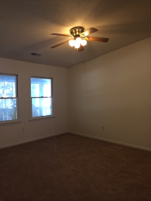 A room with a ceiling fan and two windows.