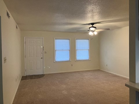 A room with a carpeted floor, a ceiling fan, and two windows.