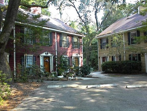 A red house with a white door and windows is surrounded by trees.