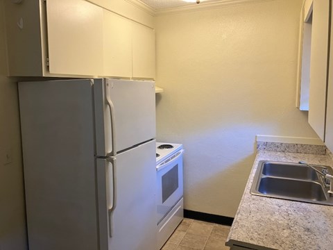 A kitchen with a white refrigerator, stove, and sink.