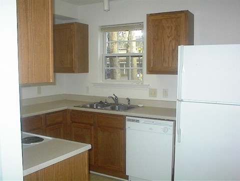 A white fridge sits in a kitchen with wooden cabinets.