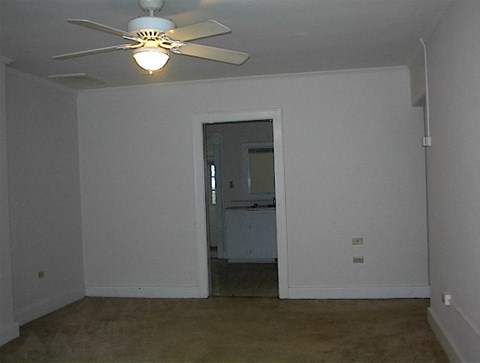 A room with a ceiling fan and a doorway leading to a kitchen.