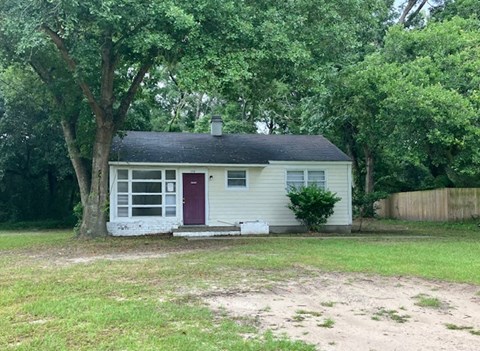 A small white house with a red door is surrounded by trees.