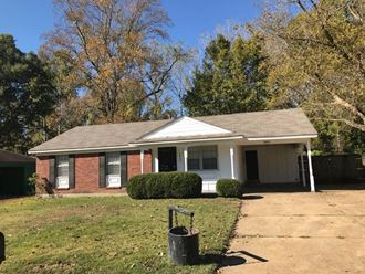 a small brick house with a driveway and trees