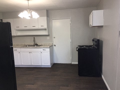 A black refrigerator is in the corner of a kitchen with white cabinets and a black trash can.