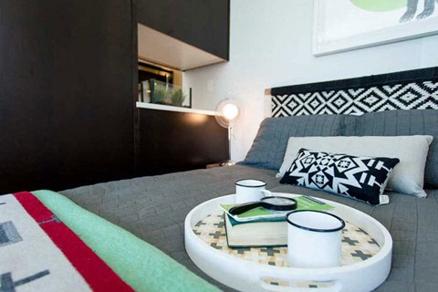 A round tray with a book and two cups on it sits on a bed.