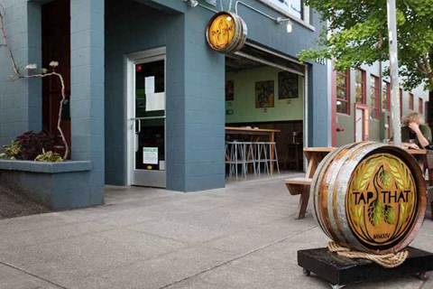 A barrel with the words "Tap That" on it is outside a building.
