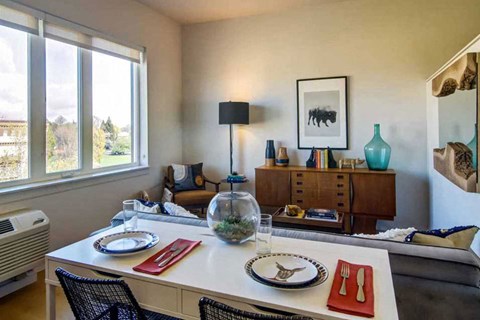 A dining room with a table set for two and a view of the outdoors through the window.