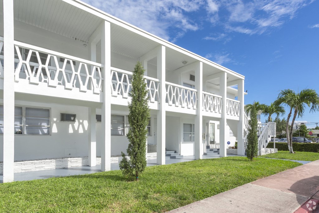 the exterior of a white house with a lawn and palm trees