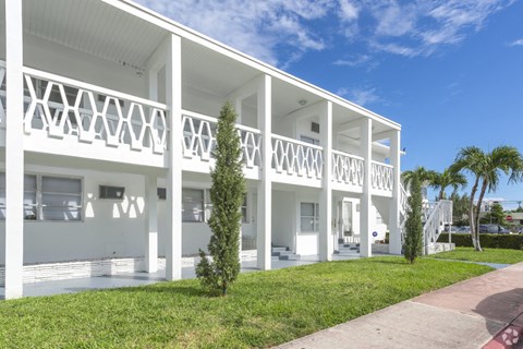 the exterior of a white house with a lawn and palm trees