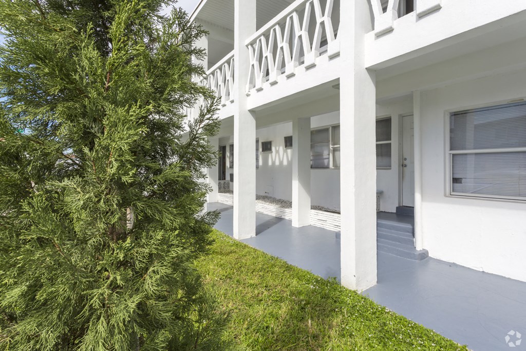 the front of a white house with a porch and a tree
