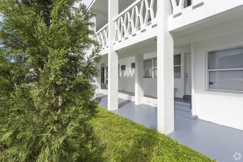 the front of a white house with a porch and a tree