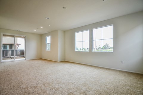 an empty living room with three windows and carpeting