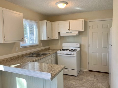A kitchen with white cabinets and a white stove top oven.