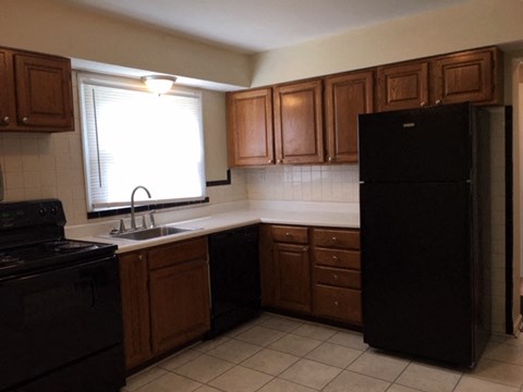 A black refrigerator stands in a kitchen with wooden cabinets and a black stove.