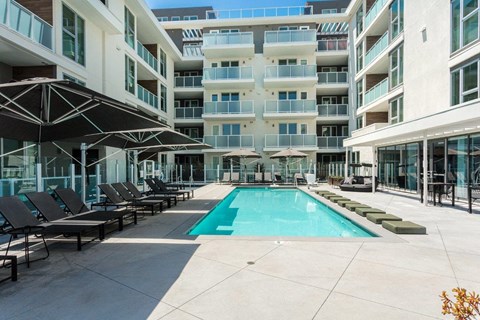 A swimming pool surrounded by lounge chairs and umbrellas in a courtyard.