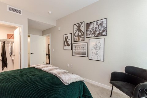 A bedroom with a green bedspread and a black chair.