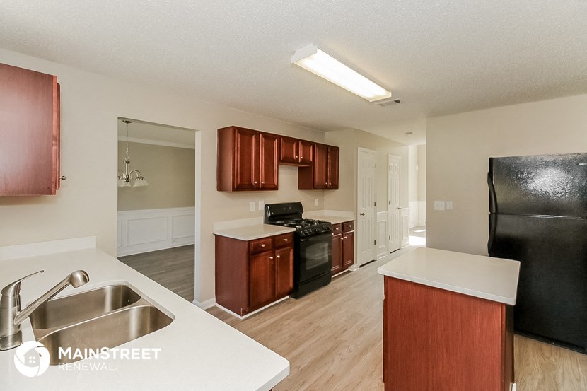 a kitchen with wood flooring and white counter tops and a black refrigerator
