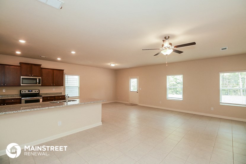 an empty living room with a kitchen and a ceiling fan