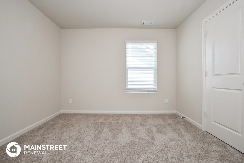 the spacious bedroom with carpeted flooring and a window