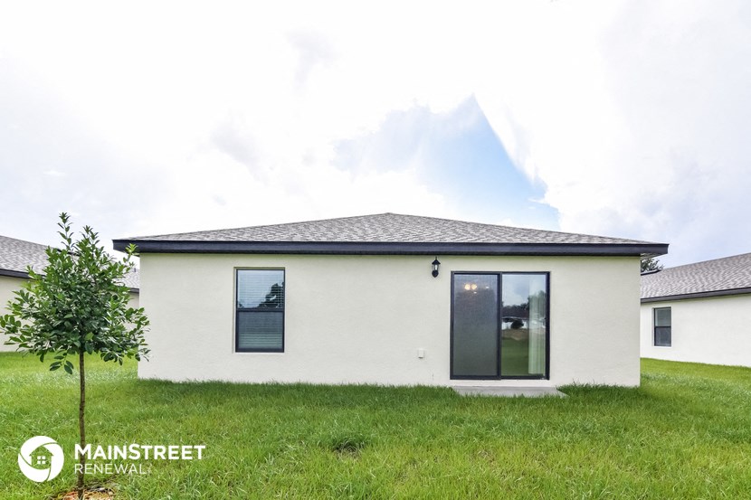the exterior of a small white home with a grassy yard and a tree