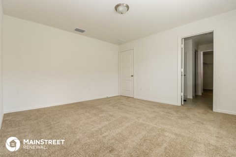a spacious living room with carpet and a door to a hallway
