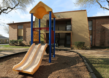 Blue and yellow playscape with climbing area and slide on woodchips. Building in background.