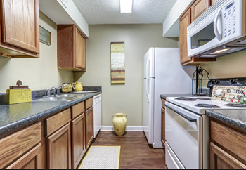 Medium brown wood flooring and cabinetry with beige walls and white appliances.