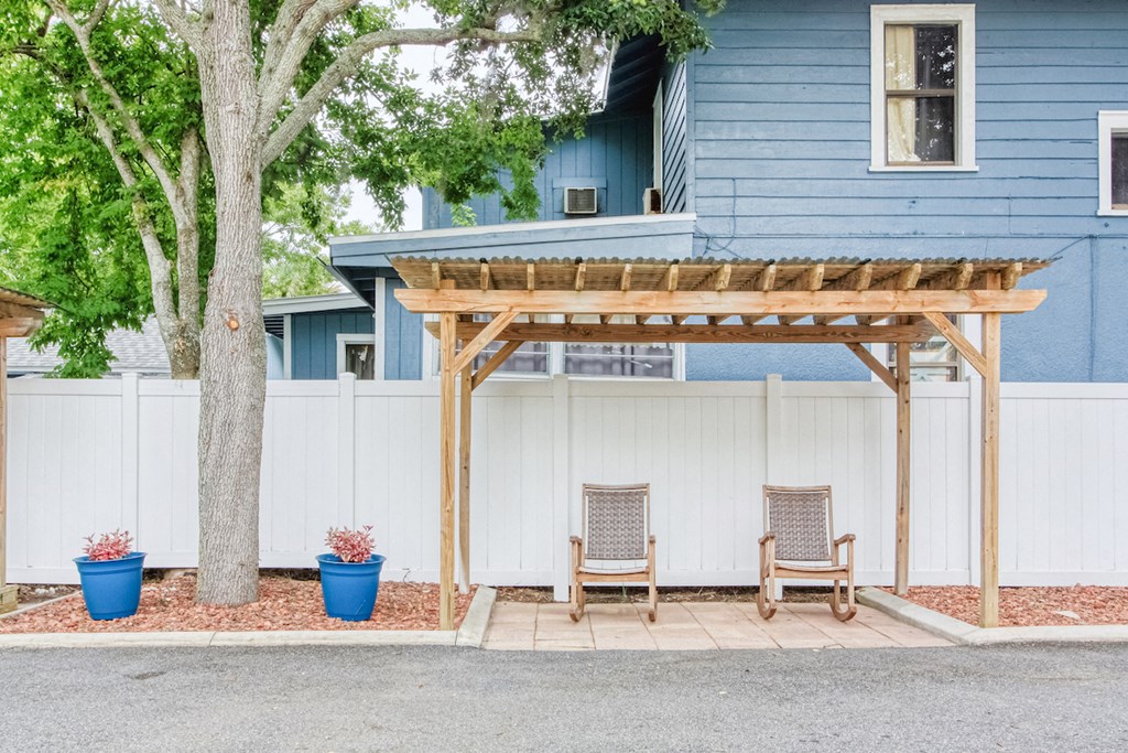 pergola with chairs beside fence with potted plants and large tree