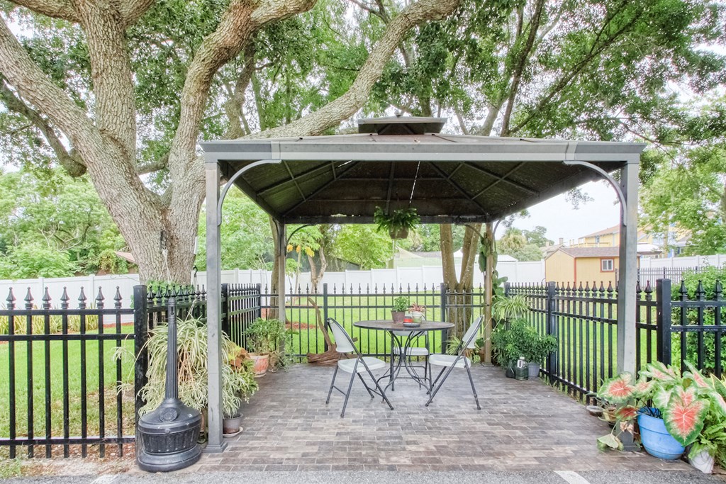 outdoor pavillion with seating under a canopy beside iron fence with potted plants
