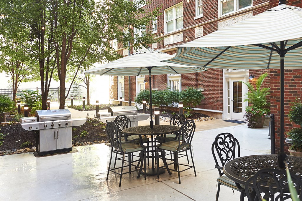Courtyard with concrete pad, black iron table with chairs, white umbrella, gas grill and trees in the background at Residences at Forest Park, Saint Louis, MO