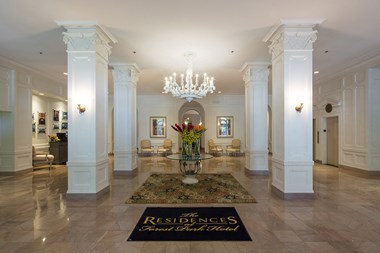 Lobby with marble tile and white chandelier over glass table.