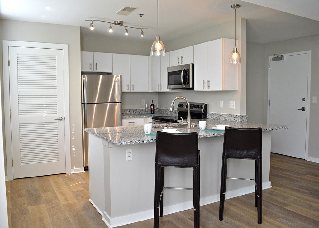 C-Shaped kitchen with white cabinets and two bar stools at Residences at Forest Park, Saint Louis, Missouri