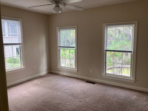 an empty room with three windows and a ceiling fan