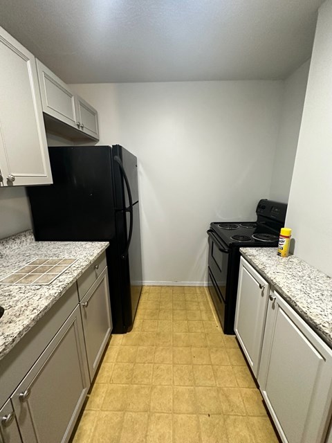 A black fridge and stove in a kitchen with white cabinets.