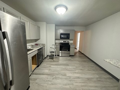 A kitchen with a refrigerator, microwave, oven, and a chair.