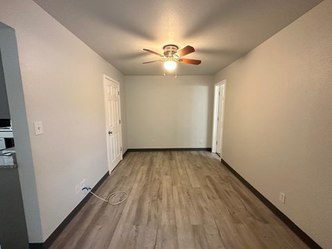 A room with a ceiling fan and light fixture, wooden flooring, and two doors.