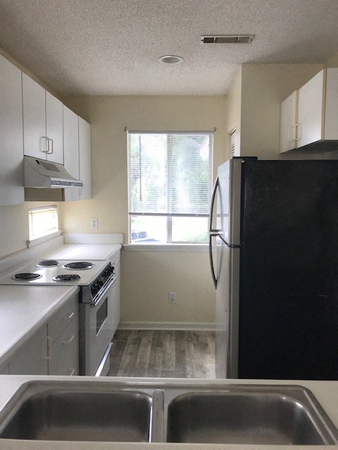 A black refrigerator sits in a kitchen with a stove and sink.