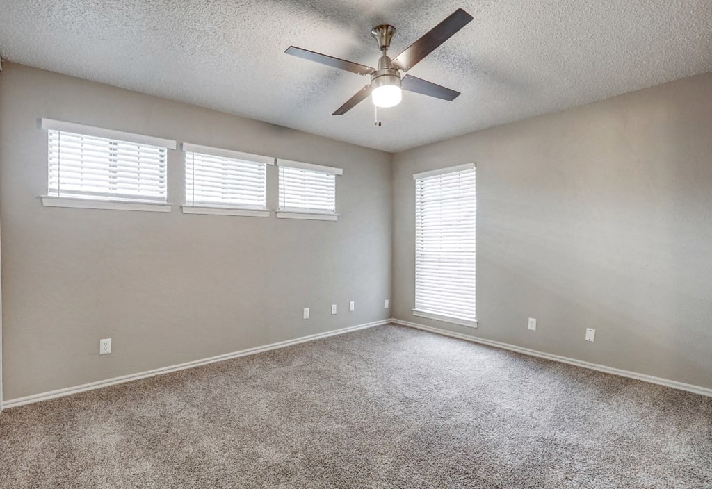 an empty living room with a ceiling fan and three windows