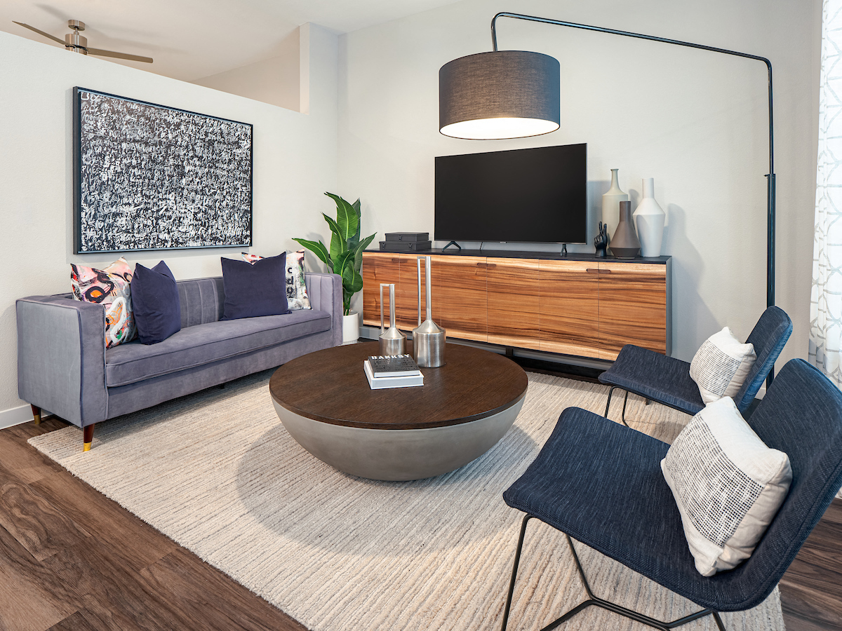 A modern living room with a grey couch, a coffee table, a TV, and a large abstract painting on the wall.