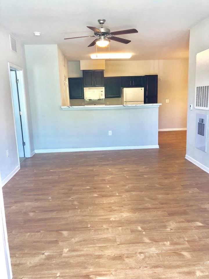 an empty living room with a ceiling fan and a kitchen