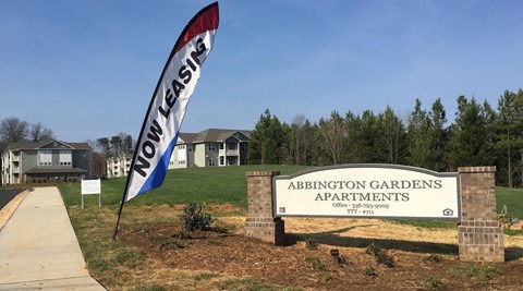 a sign for adoption gardens apartments in front of a field with trees