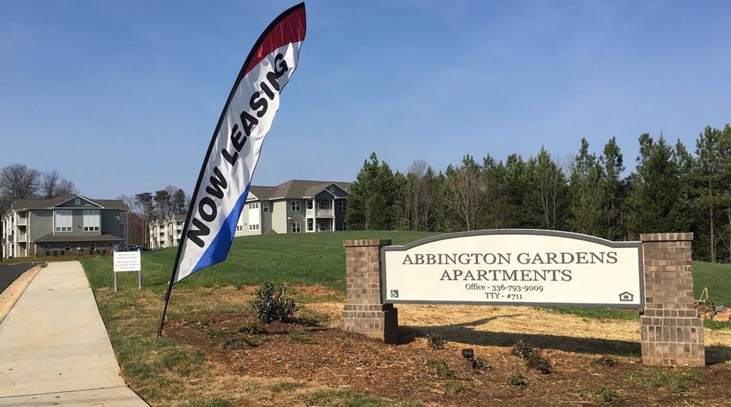 a sign for adoption gardens apartments in front of a field with trees