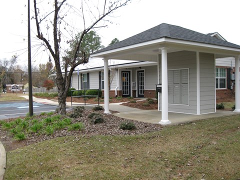 A small house with a porch and a tree in front.
