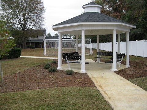 A gazebo with a white fence and benches in front of a house.